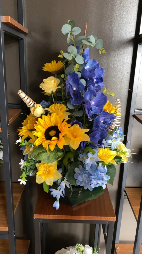 Composition florale funéraire avec tournesols jaunes et fleurs bleues.
