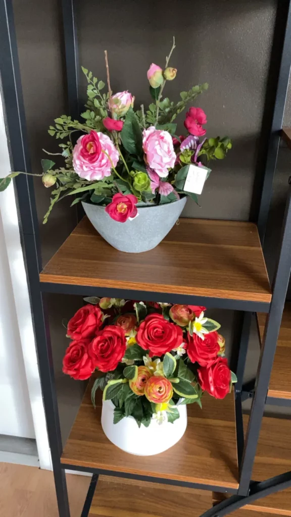 Bouquets de fleurs artificielles roses et rouges disposés sur une étagère.