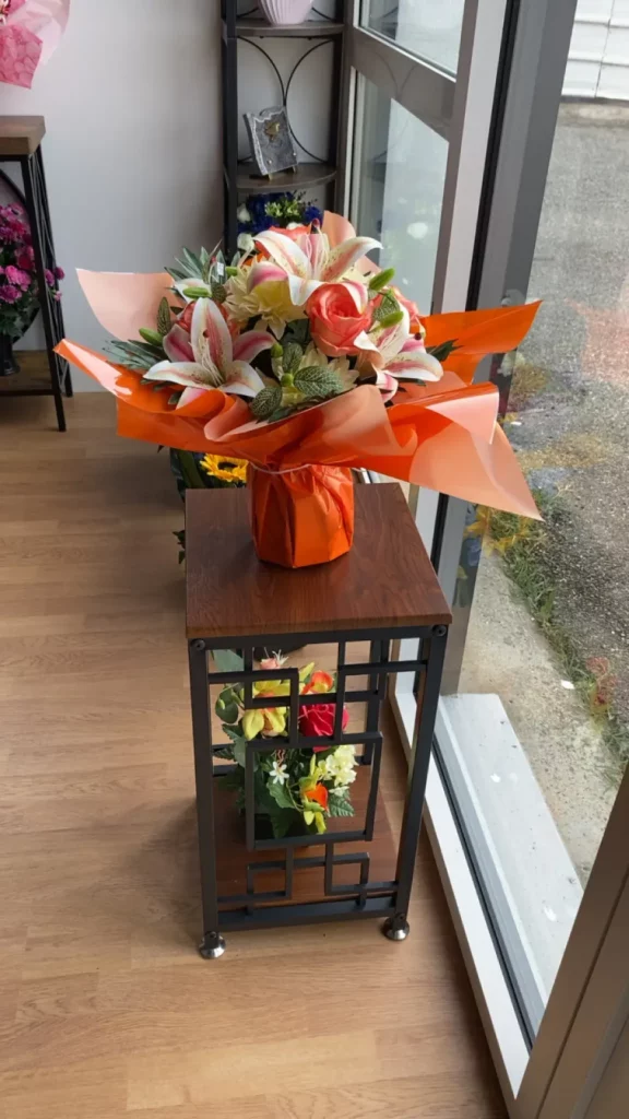 Grand bouquet de lys et roses deuil emballé dans du papier orange.